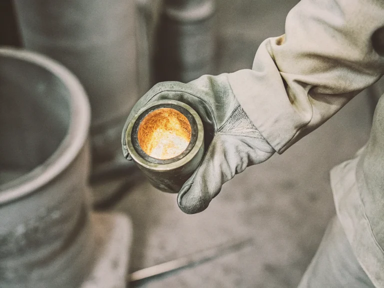 Процесс аффинажа золота: рабочий держит тигель с расплавленным металлом на заводе