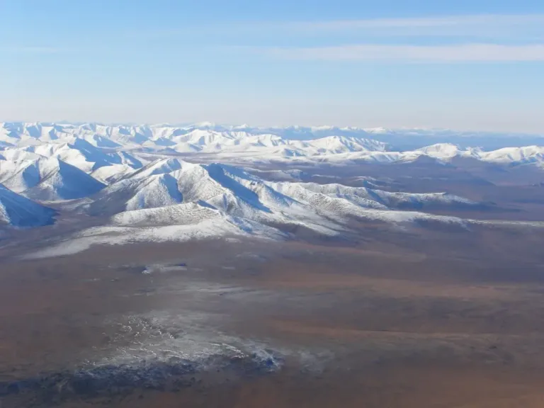 Заснеженные холмы в зоне вечной мерзлоты, где из-за потепления увеличивается глубина сезонного протаивания и грунт теряет устойчивость.