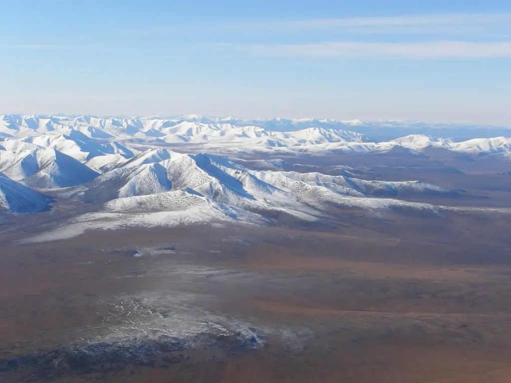 Заснеженные холмы в зоне вечной мерзлоты, где из-за потепления увеличивается глубина сезонного протаивания и грунт теряет устойчивость.
